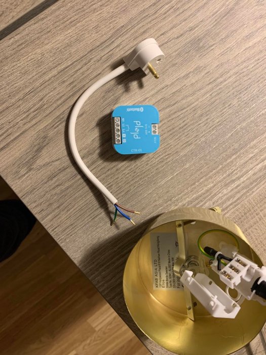 Eluttag, avslutad kabel, blå kopplingsdosa, demonterad guldfärgad lampfot på ett träbord.