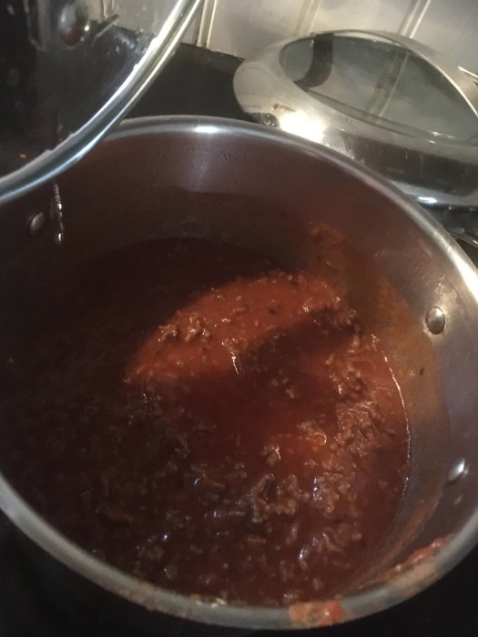 En gryta med köttfärssås på spisen, lock lyfts, ångor, hemlagad matlagning.
