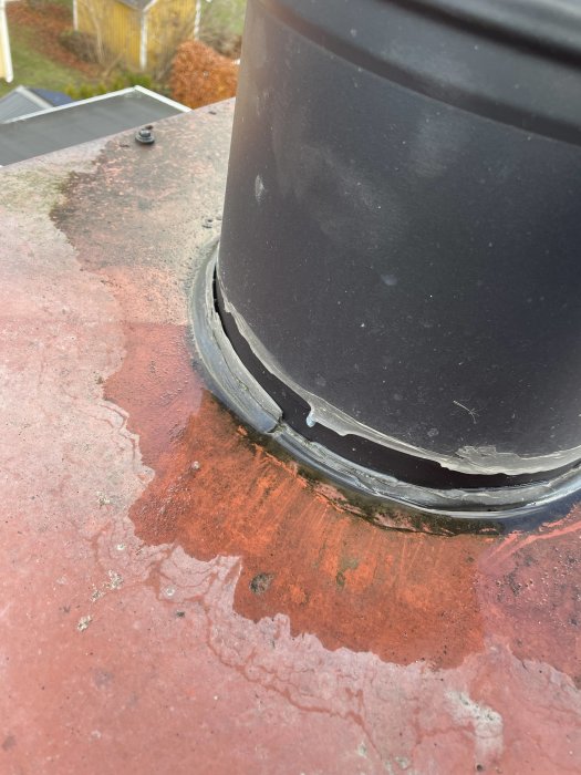 Svart ventilationsrör genom rött tak, tätning, möjlig vatteninträngning, rost, slitage.