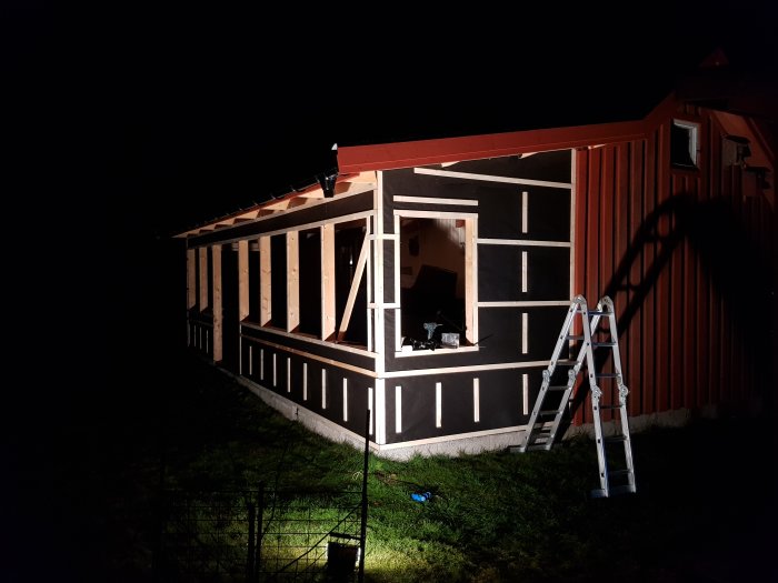 Ett rött hus under konstruktion i nattbelysning med stege och skuggor.