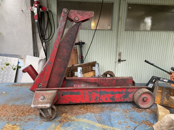 Röd pallbock på sliten metallplatta, verktyg i bakgrunden, industriell miljö, använd och sliten utrustning.