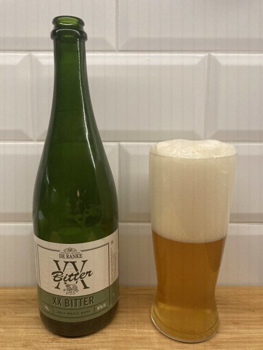 Grön ölflaska och ett glas med öl och tjockt skum på köksbänk.