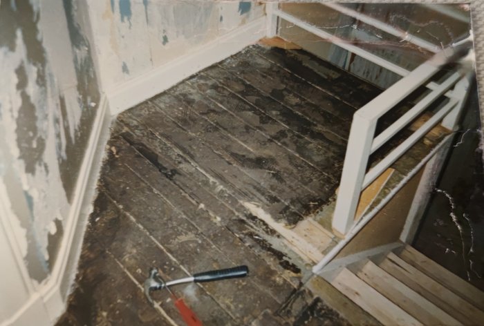 Renoveringsarbete i rum, gamla trägolv med repor, verktyg på golvet, oavslutade väggar, trappräcke.