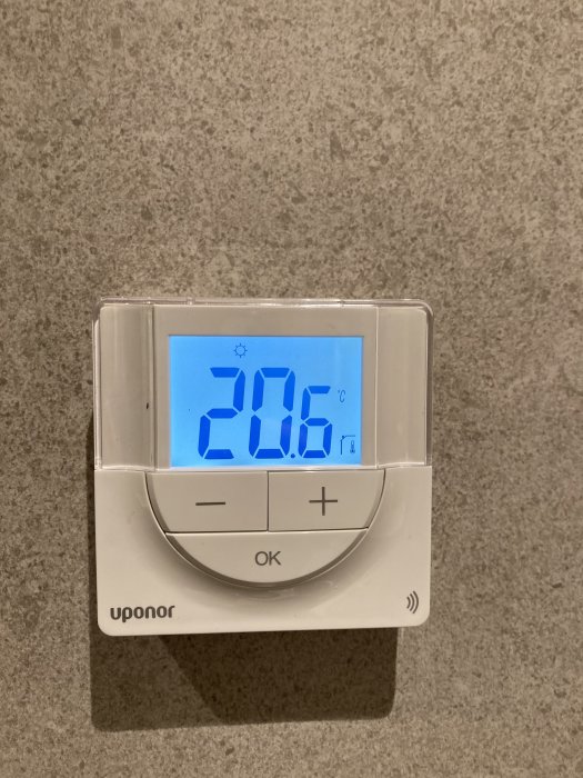 Digital termostat på vägg visar 20.6 grader Celsius, justeringsknappar, märke 'Uponor'.