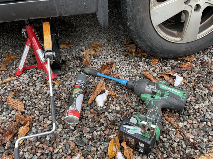 Bilverktyg på marken, däckbyte, domkraft, momentnyckel, batteridriven slagnyckel, rostlösningsmedel, höstlöv.