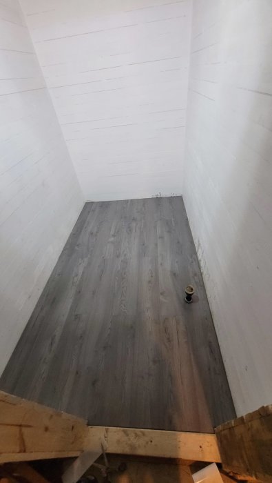Övergivet rum, trägolv, vita väggar, ensam flaska på golvet, nedtaget från en trappavsats.