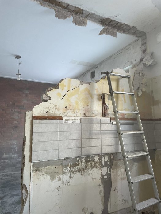 Renoveringsprojekt; skadat tak, riven vägg, stege, delvis kaklad vägg, råa material synliga, byggarbetsmiljö.