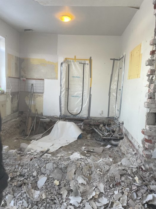 Rum under renovering med rörmokararbete, rivna väggar och byggavfall utspridda över golvet.