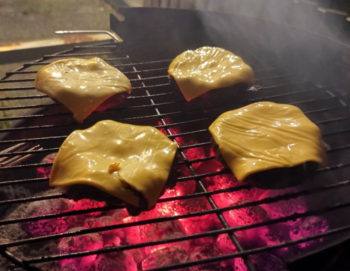 Fyra hamburgare med ost på grillen; varm, smältande, grillkväll, god matlagning utomhus.