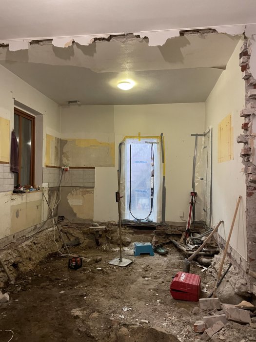 Inomhusrenovering pågår, väggar nedrivna, rör utsatta, verktyg och byggmaterial synliga, oavslutat arbete.