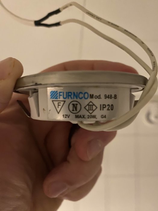En hand håller en FURNCO modell 948-B lampsockel etiketterad med tekniska specifikationer som IP20 och 12V.