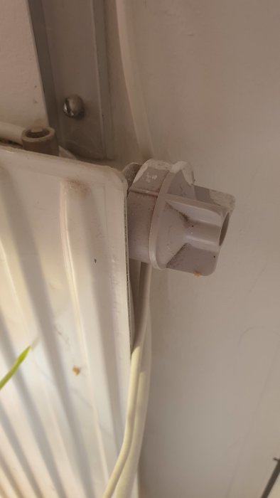 En vit termostatventil på radiator, kablar löper nära, inomhus, närbild, lite dammigt.