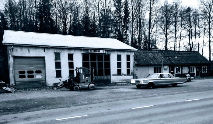 Svartvit bild, äldre byggnad med skylten "Trelleborg", klassisk bil, gaffeltruck, lantlig miljö, övergivet utseende.