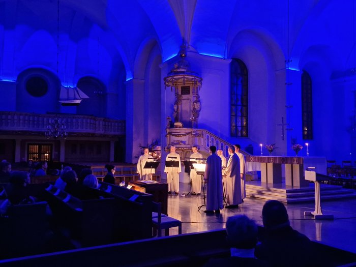 Kör uppträder i kyrka med blått ljus, åhörare lyssnar. Stämningsfullt, lugnt, religiös musik.