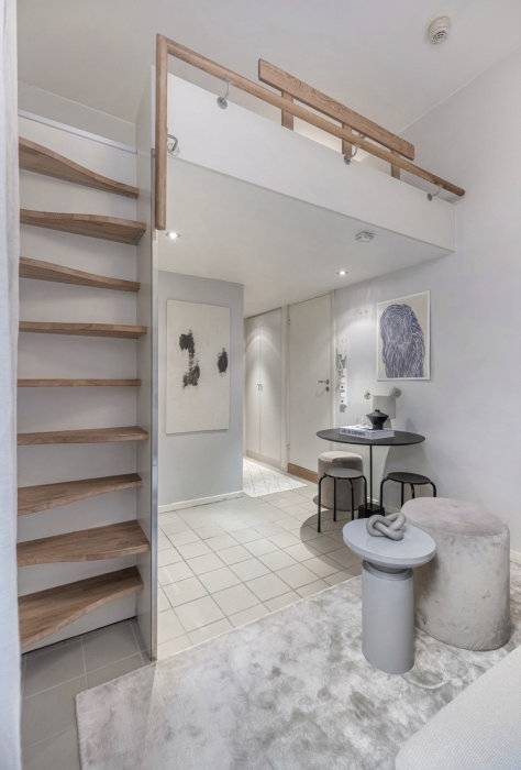 Modernt vardagsrum med trätrappa, vit inredning, konst, och minimalistiska möbler.