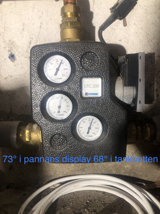 Värmesystemskomponent med mätare, rörkopplingar, text "73° i pannans display 68° i tankbotten".