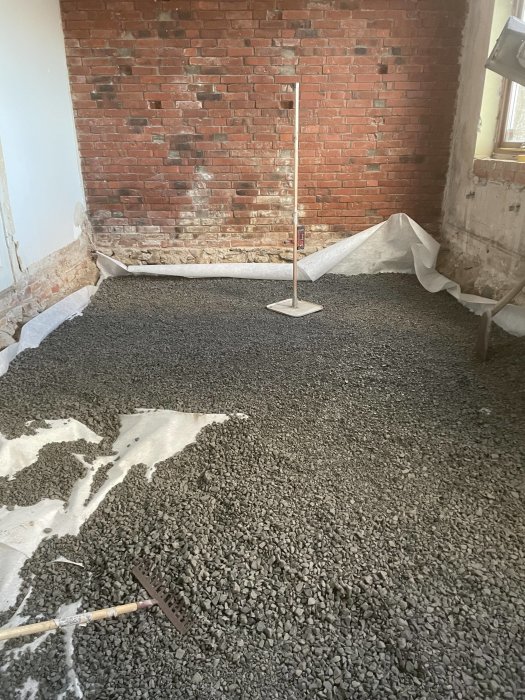 Renovering inomhus, rödfärgad tegelvägg, utjämnad grusgolv, stödpelare mitt i rummet, byggmaterial, fiberduk.