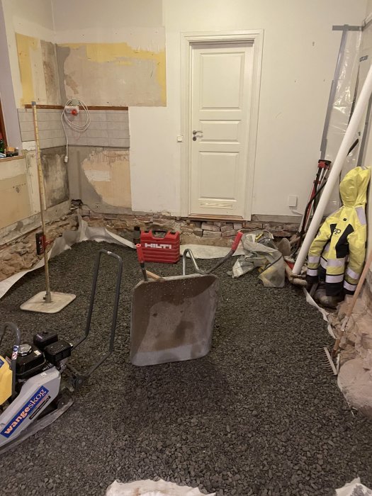 Renoveringsarbete pågår, rör och verktyg syns, vägg delvis avtäckt, skivad sten golvet, uppbruten yta, byggstök.