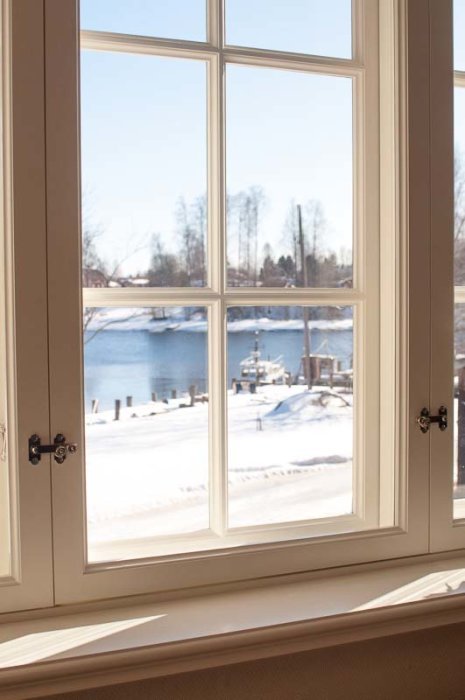 Ett fönster med utsikt över en snöig landskap och en frusen sjö under en klar himmel.