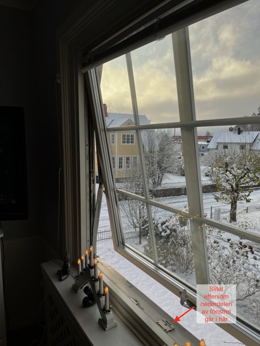 Öppet fönster, adventsljusstake, snötäckt utsikt, gula hus, vinterdag, skylt om slitage på fönstret.