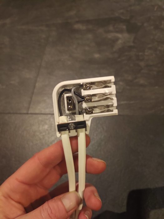 En hand håller en vit elektrisk kabel med avskalad slutdel och synliga koppartrådar.