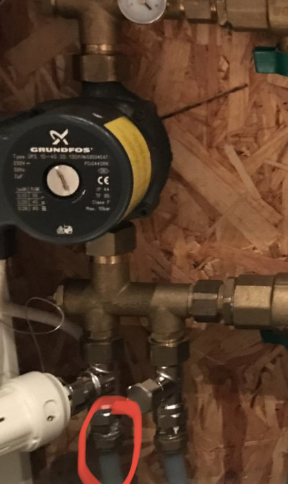 Rörsystem med Grundfos cirkulationspump, ventiler, mätare mot en flisvägg. Röd markering kring en detalj.