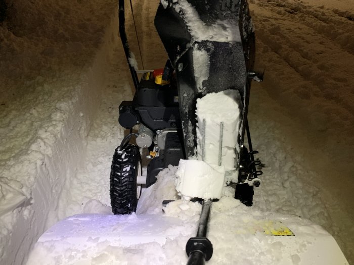 Snöslunga i arbete på natten, snöväggar på sidorna, tjockt snötäcke.