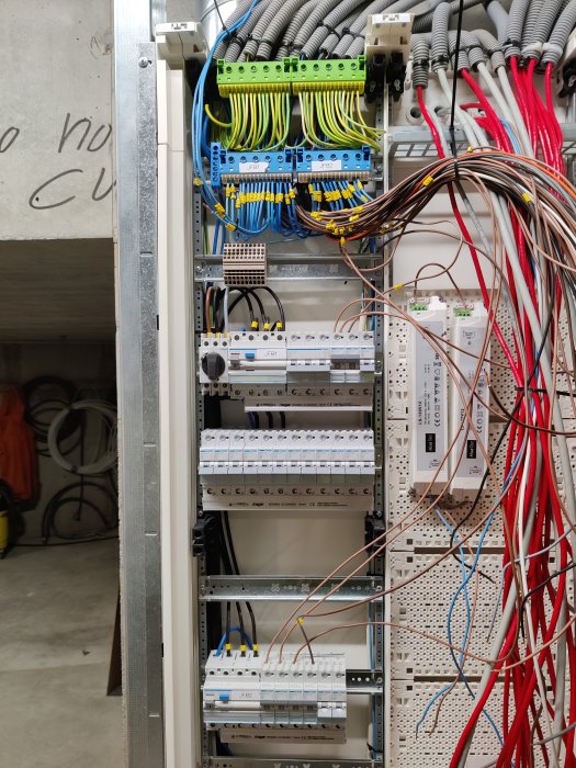Elektriskt skåp med strukturerade och ostrukturerade kablar, säkringar, och kopplingspanel i industriell miljö.