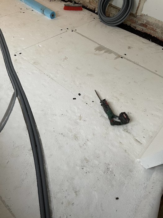 Renoveringsplats, oavslutat golv, verktyg, byggmaterial, sladdar, skräp.