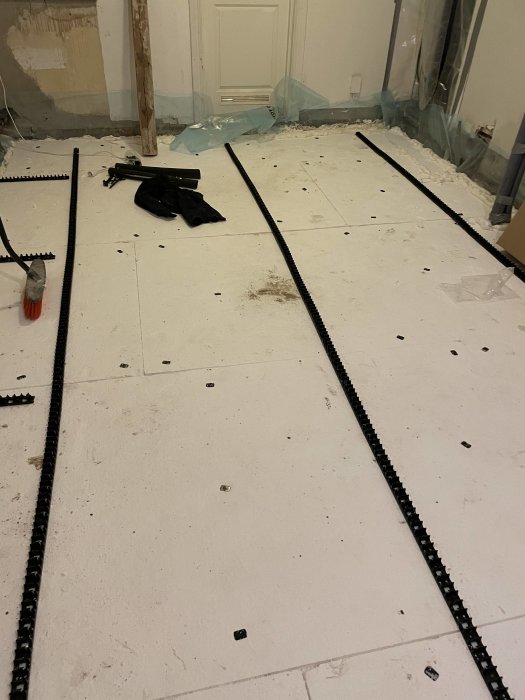 Omfattande renovering, isolerad golvyta, kablar och rör, verktyg och byggmaterial synliga, ofärdigt rum.