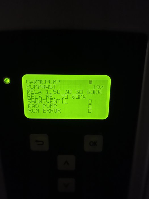 Grön bakgrundsbelyst LCD-panel som visar driftinformation för värmepumpssystem. Knappar markerade med symboler nedanför displayen.