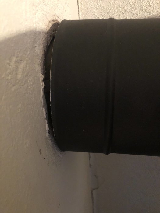 Svart rör mot vit vägg, inuti ett hål med spruckna kanter.