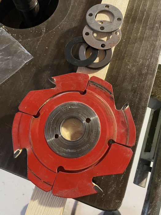 Röd fräsverktyg med tungstenkarbid sitter på en arbetsbänk bredvid andra metalkomponenter.