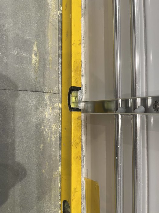 Bild av gult stötskydd och grå metallrör nära en betonggolv och vägg.