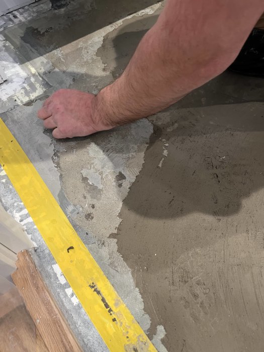 Person utför betongarbete eller golvavjämning inomhus; detalj av arm och hand; byggarbetsplats; renovering.