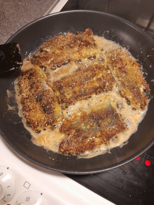 Panerade schnitzlar steks i panna på spis, gyllenbruna, fräser i olja.