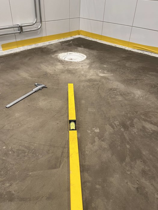 Ett golv under konstruktion med vattenpass, gula markeringar och synlig avloppsbrunn.