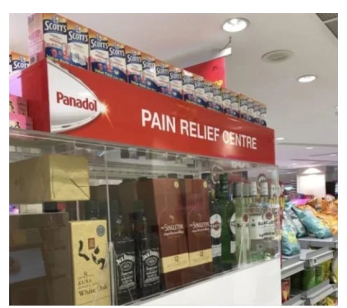 Butikshylla: "PAIN RELIEF CENTRE" skylt, uppställd ovanför alkohol. Ironi eller placeringstavla.