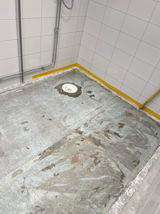 Ett duschutrymme under renovering med avlägsnat golv och exponerad avlopp.