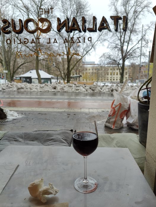 Vin i glas framför fönster med utsikt över snötäckt gata, omkastad text på fönstret visar restaurangnamn.