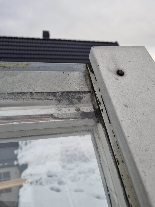 Fönsterhörn med smuts, snö bakgrund, svart föremål på fönsterkarm, tak i dis.