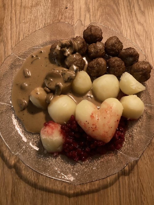 Svenska köttbullar, potatis, lingonsylt och gräddsås serverat på genomskinligt fat.