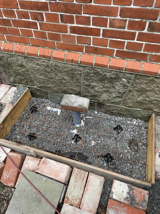 Grundarbete för byggnation, murverk, armeringsjärn, sten, rör, tegelsten, grus, träform.