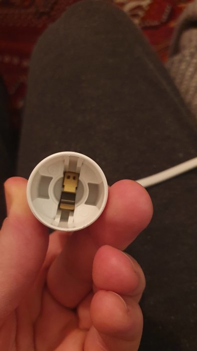 Person håller en öppen laddningskapsel med USB-kontakt, vit kabel, interiör synlig, närbild.