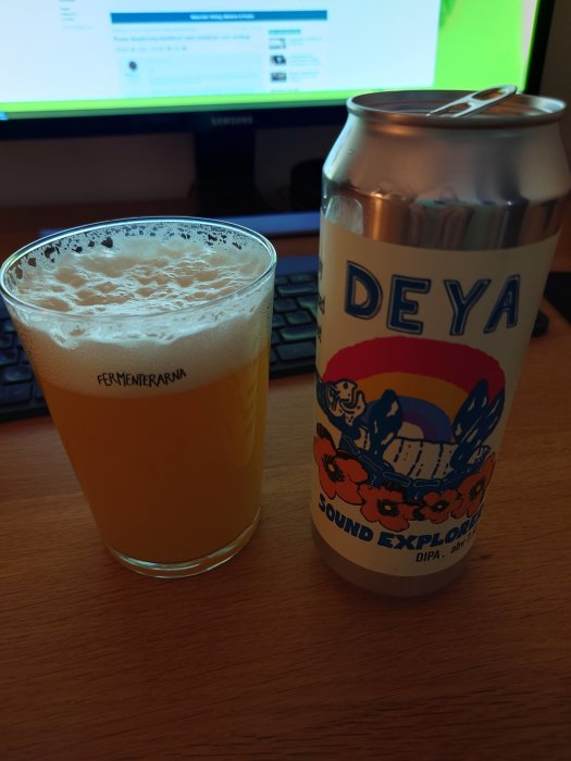 Glas med öl, färgglad ölburk, datortangentbord, skärm med webbsida i bakgrunden.