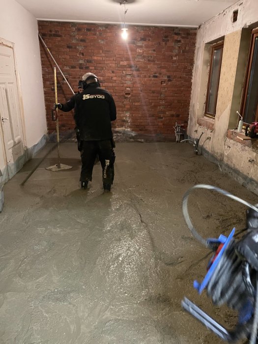 Arbetare nivellerar våt betong i renoverat rum med röd tegelvägg.