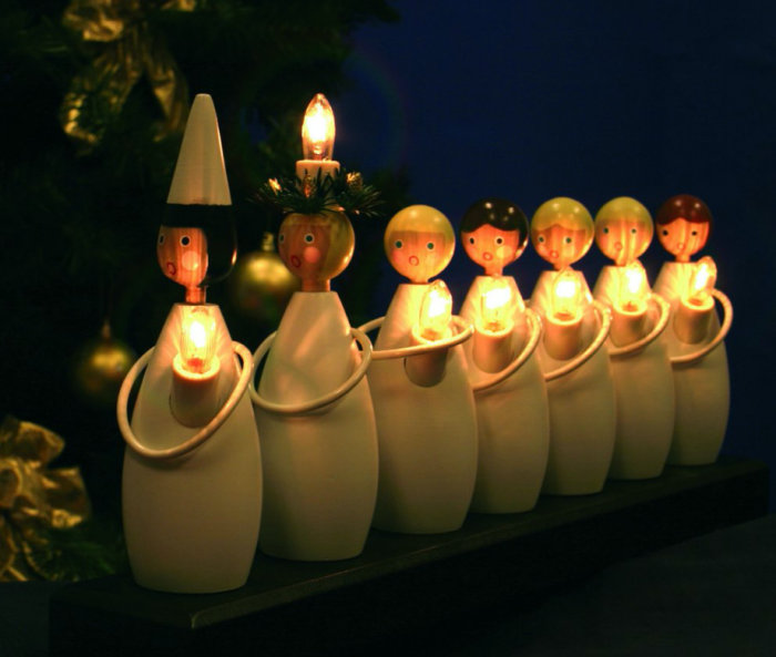 En rad traditionella svenska adventsljusstakar som gestaltar Luciatåget, med tända ljus, i mörk bakgrund.