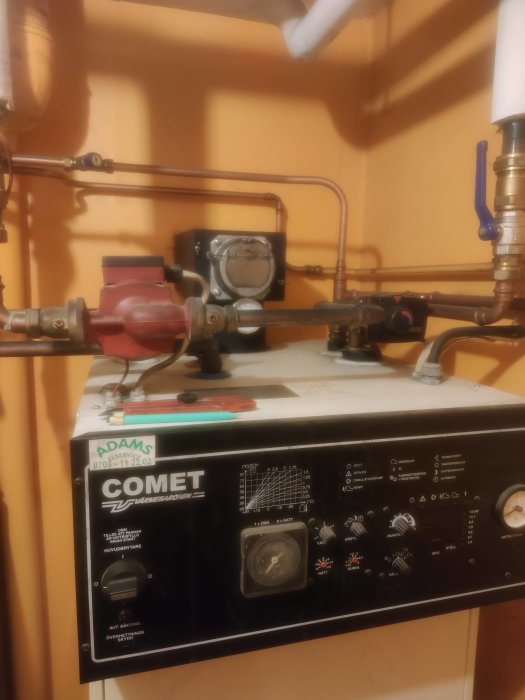 Värmeanläggning med rör, mätare och kontrollpanel, märkt "COMET," i tekniskt utrymme.