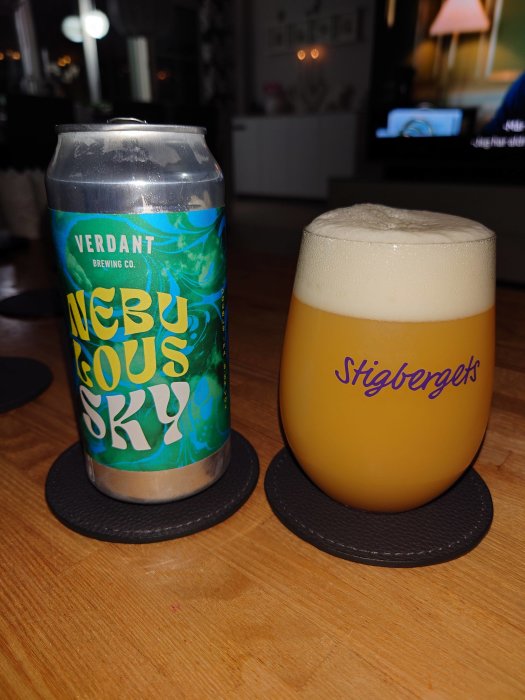 Ölburk och glas med skummande öl på träbord, underlägg, bakgrund med inredning och TV.