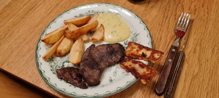 En måltid med stekt kött, pommes frites, haloumi och bearnaisesås på ett mönstrat fat.